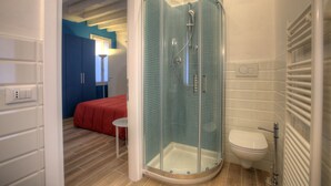 A modern bathroom with a glass-enclosed shower, a white toilet, and a red bed in the background. - Ca Sarasina (Venice)
