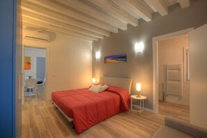 A bedroom with a bed, bedside lamps, a painting on the wall, and a bathroom with a towel rack. - Ca Sarasina (Venice)