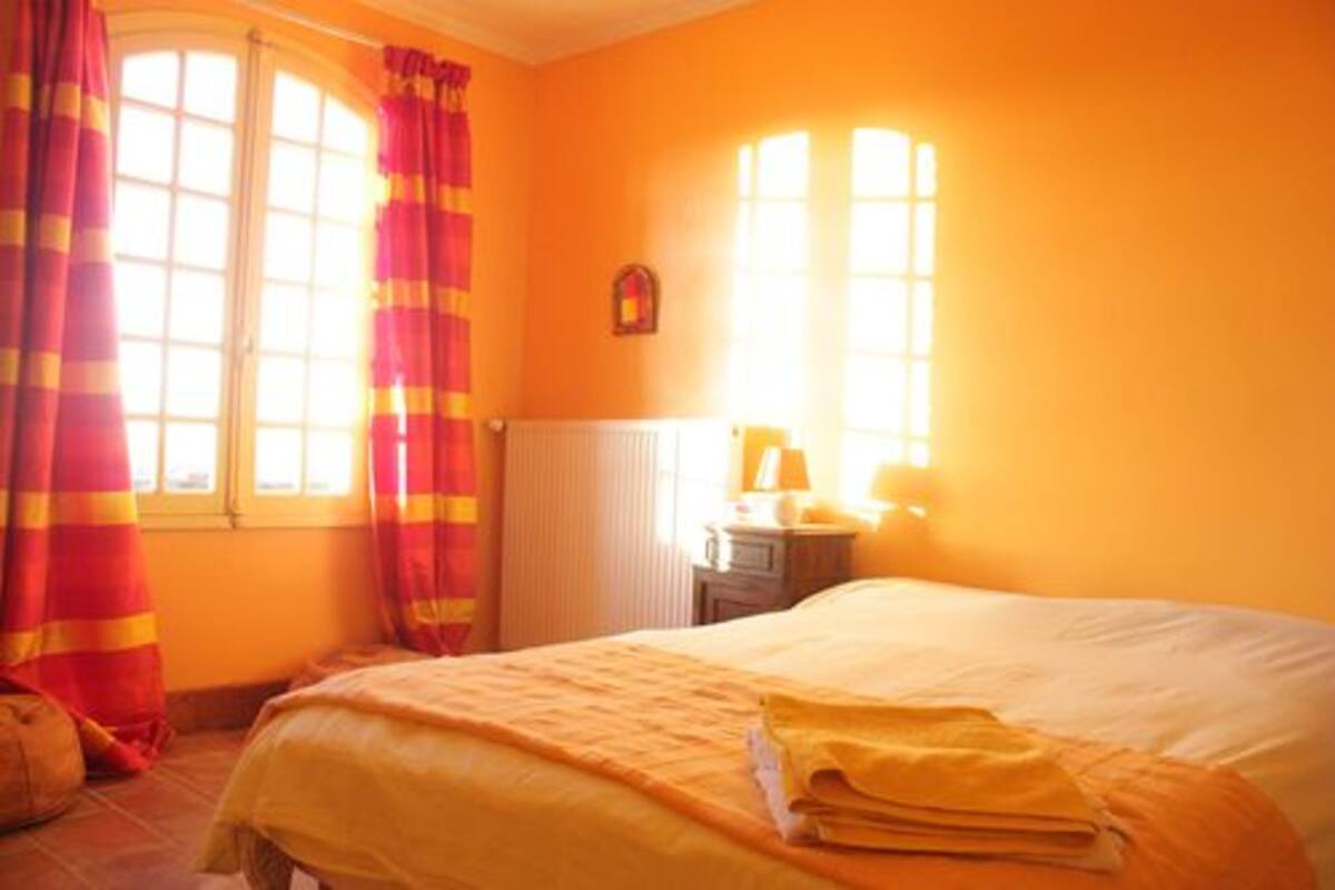 Une pièce avec un lit, un radiateur et une fenêtre avec des rideaux.