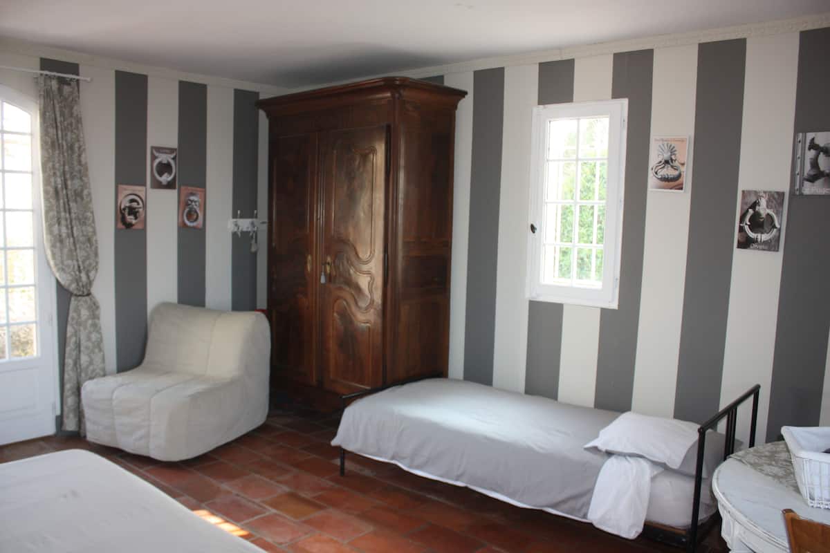 Une pièce aux murs rayés, avec une armoire en bois, un lit simple, une chaise et une fenêtre.