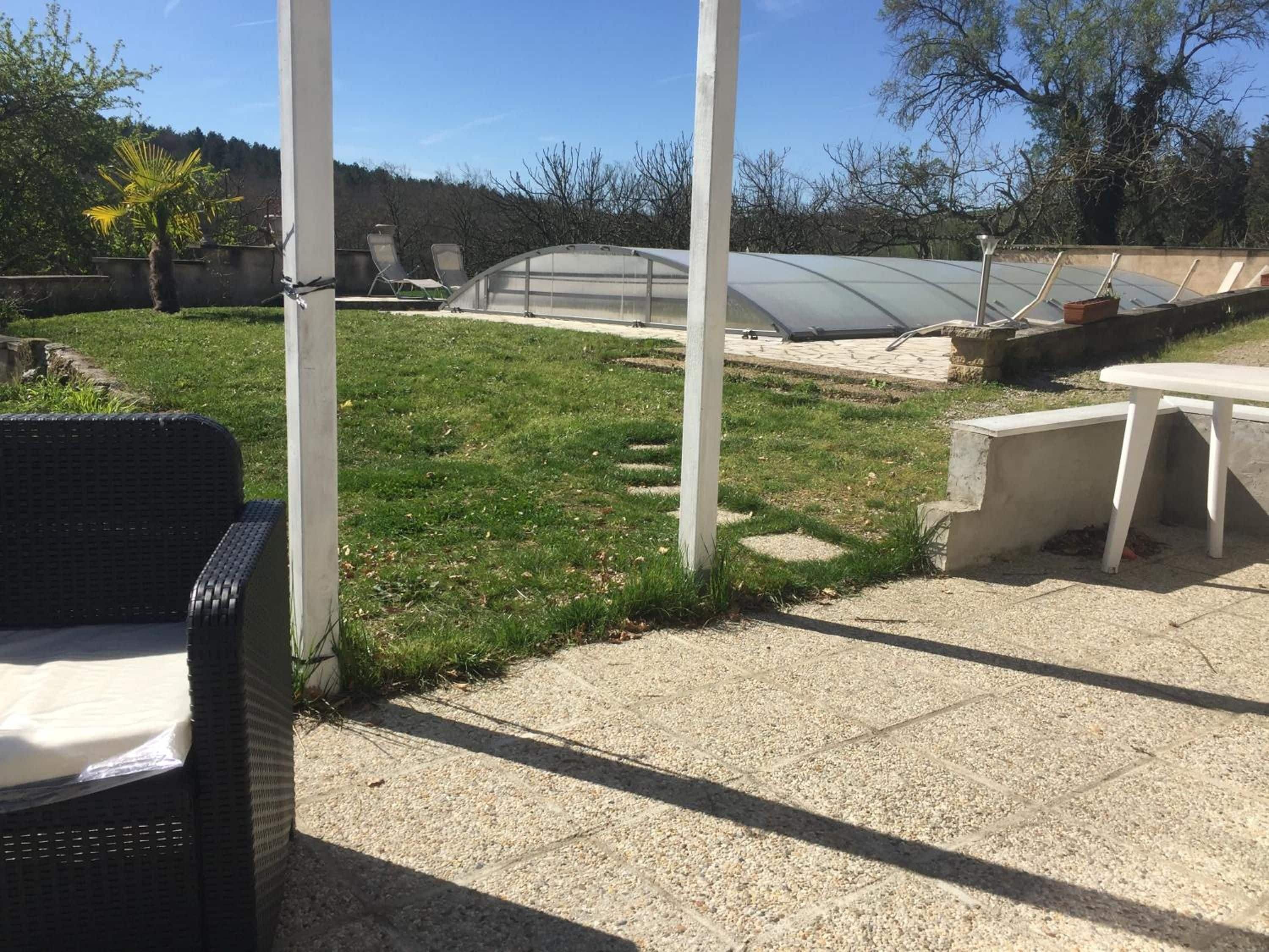 A patio area with a table and chairs, a grassy lawn, and a greenhouse structure.