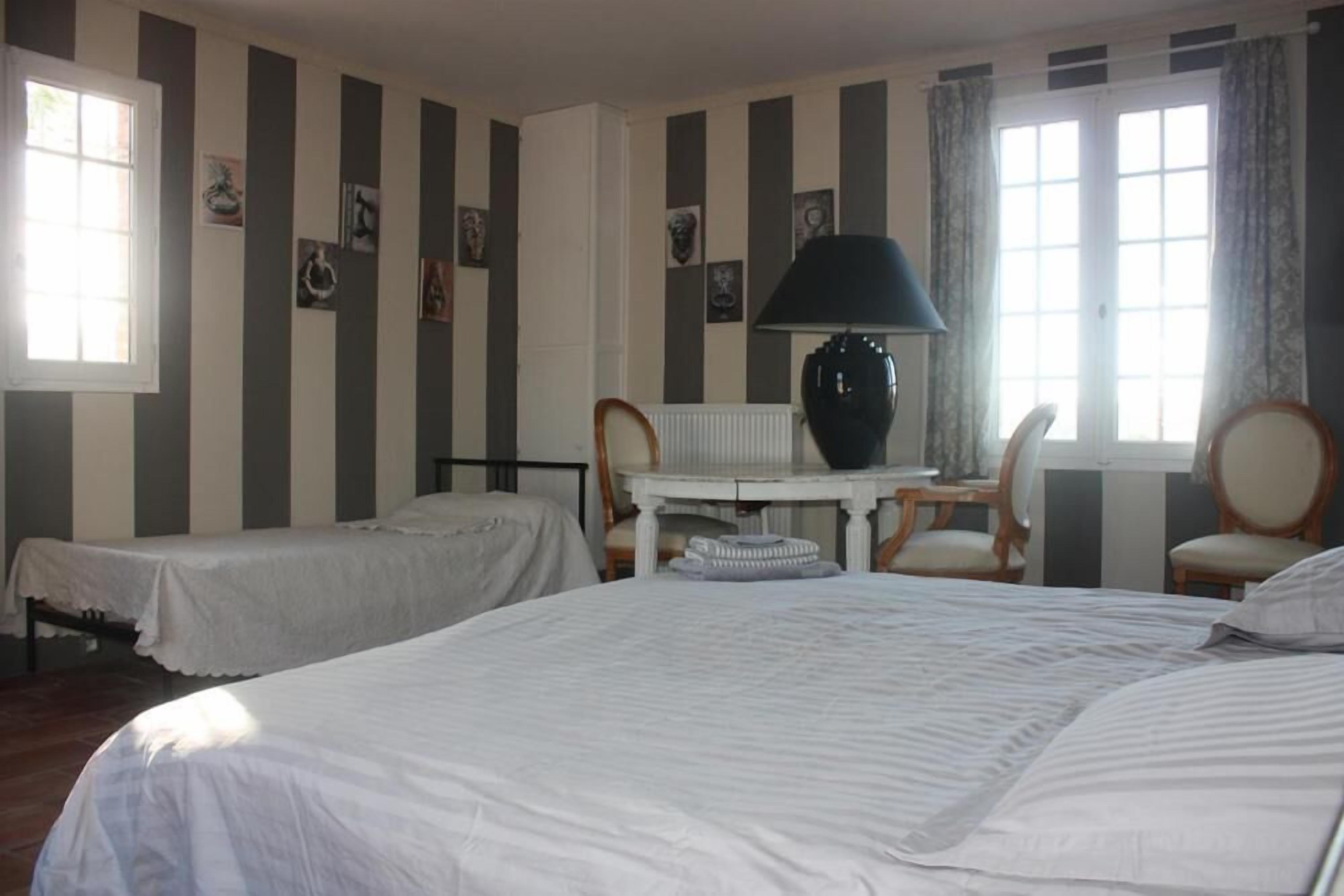 A hotel room with two single beds, a small table with a lamp, and a chair.