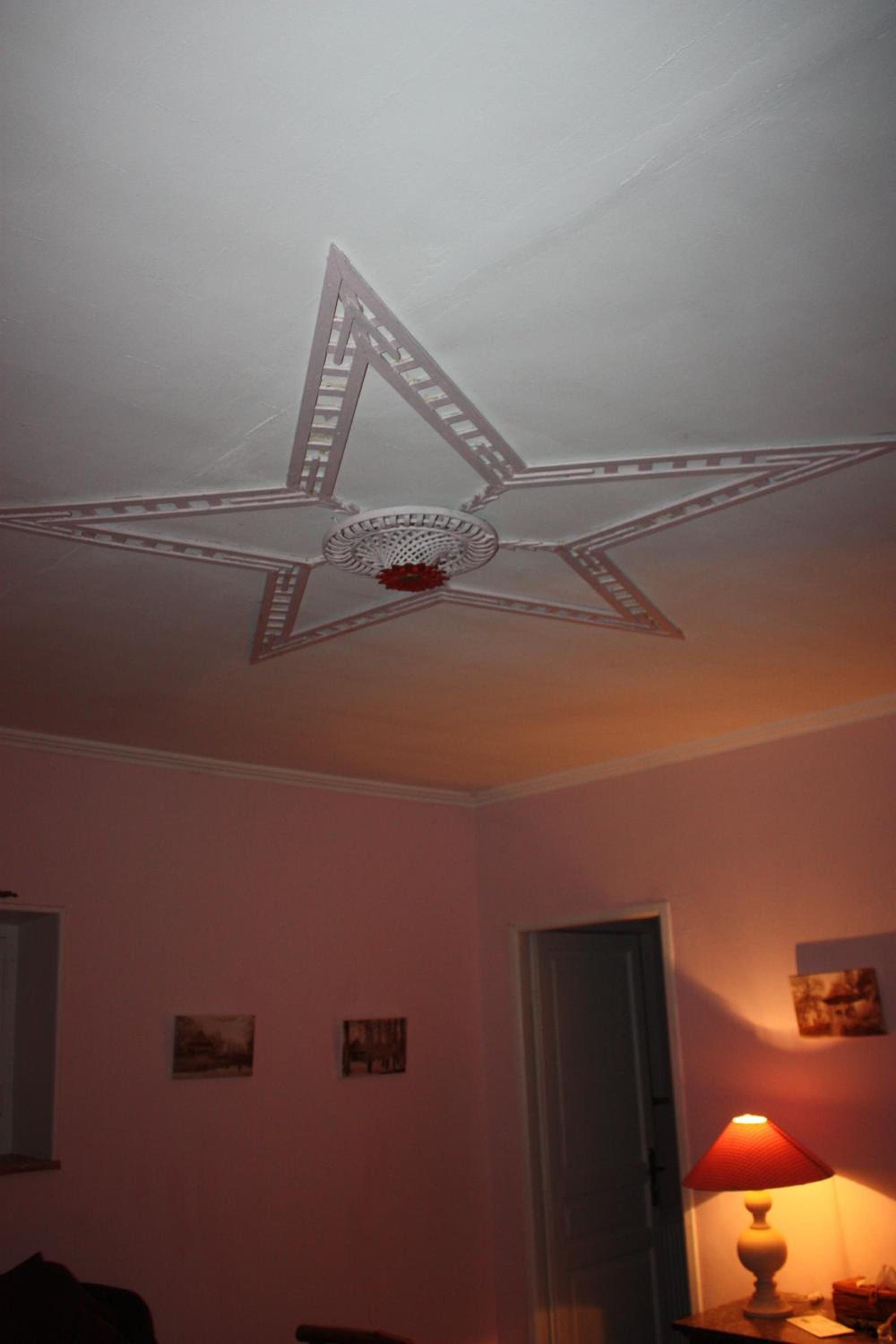 A room with a star-shaped ceiling fan, a door, and a table with a lamp.