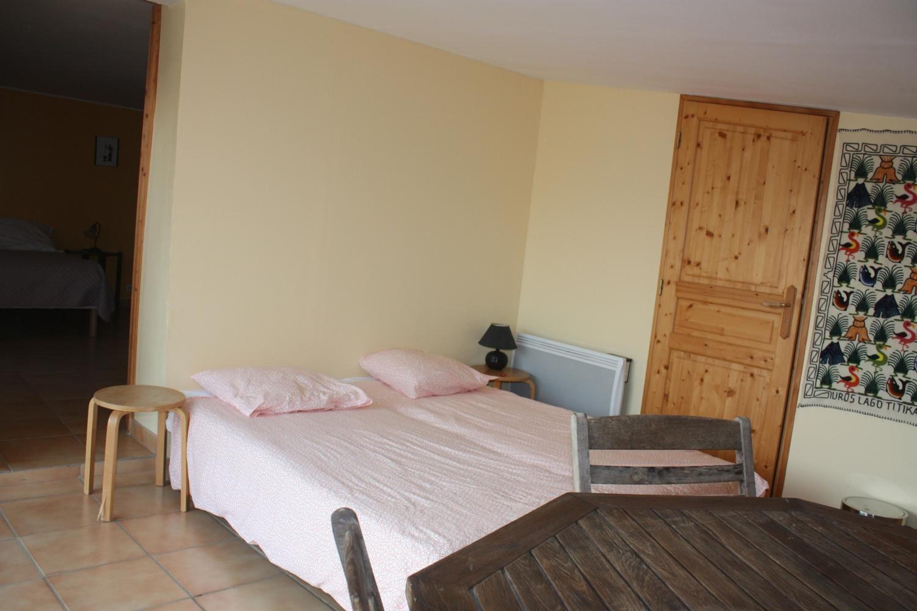 Un dormitorio con cama, una silla de madera, una mesita y una puerta con cortina estampada.
