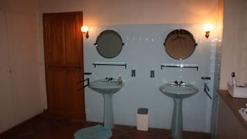 A bathroom with two sinks, a wooden door, and a trash bin.