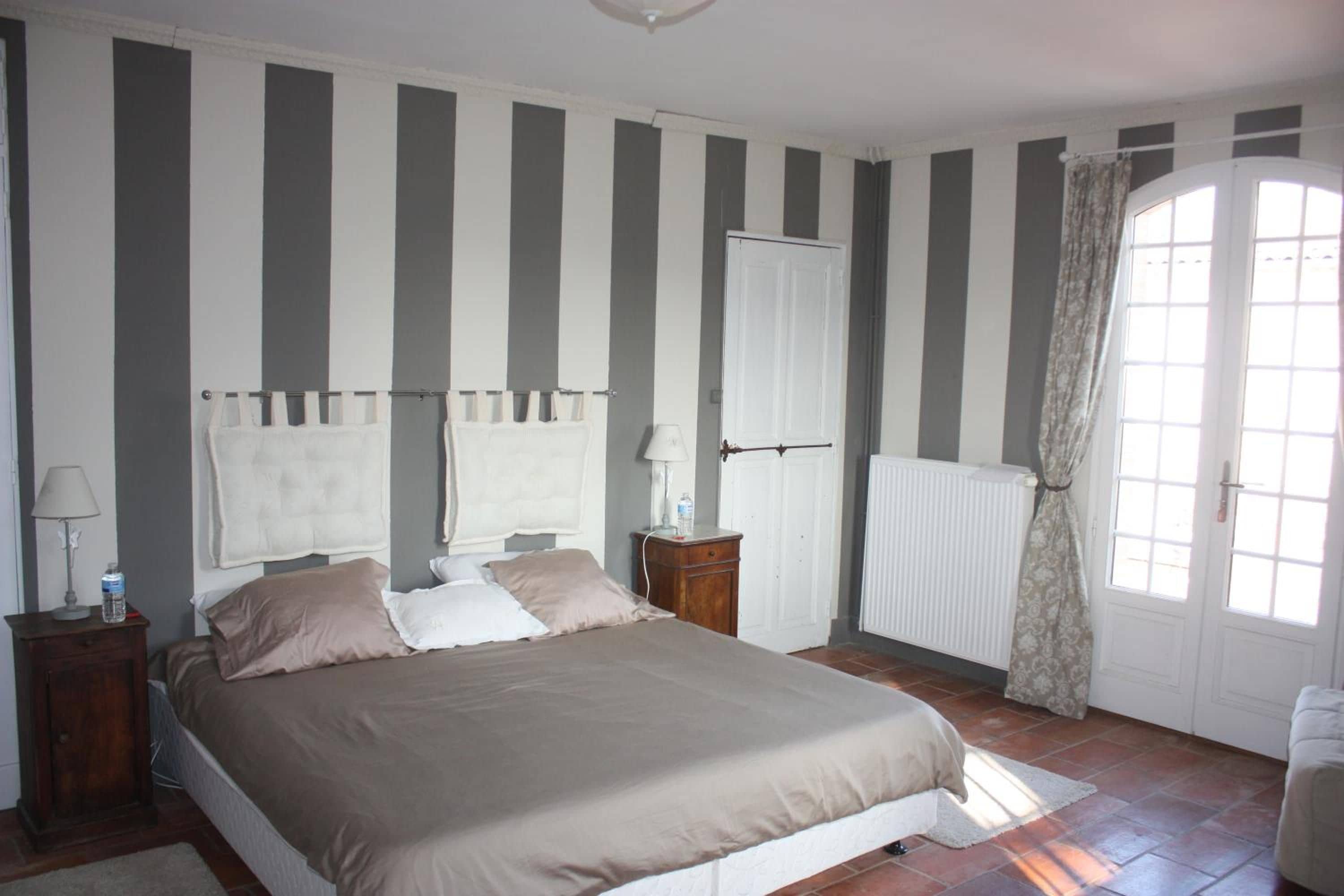 A bedroom with a bed, two bedside tables, a radiator, and a window with curtains.