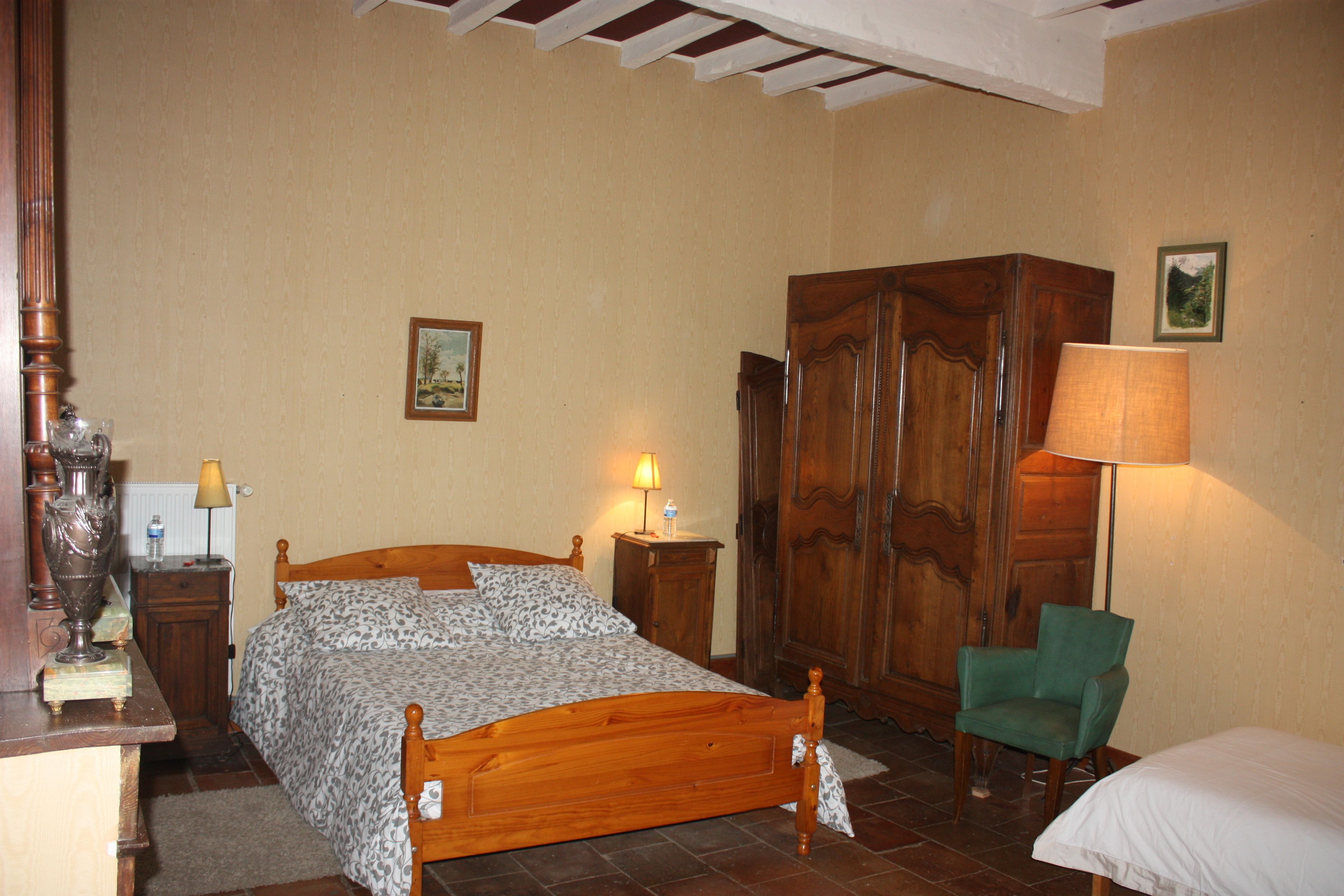 Une chambre à coucher avec un lit en bois, un fauteuil vert, une armoire et une lampe.