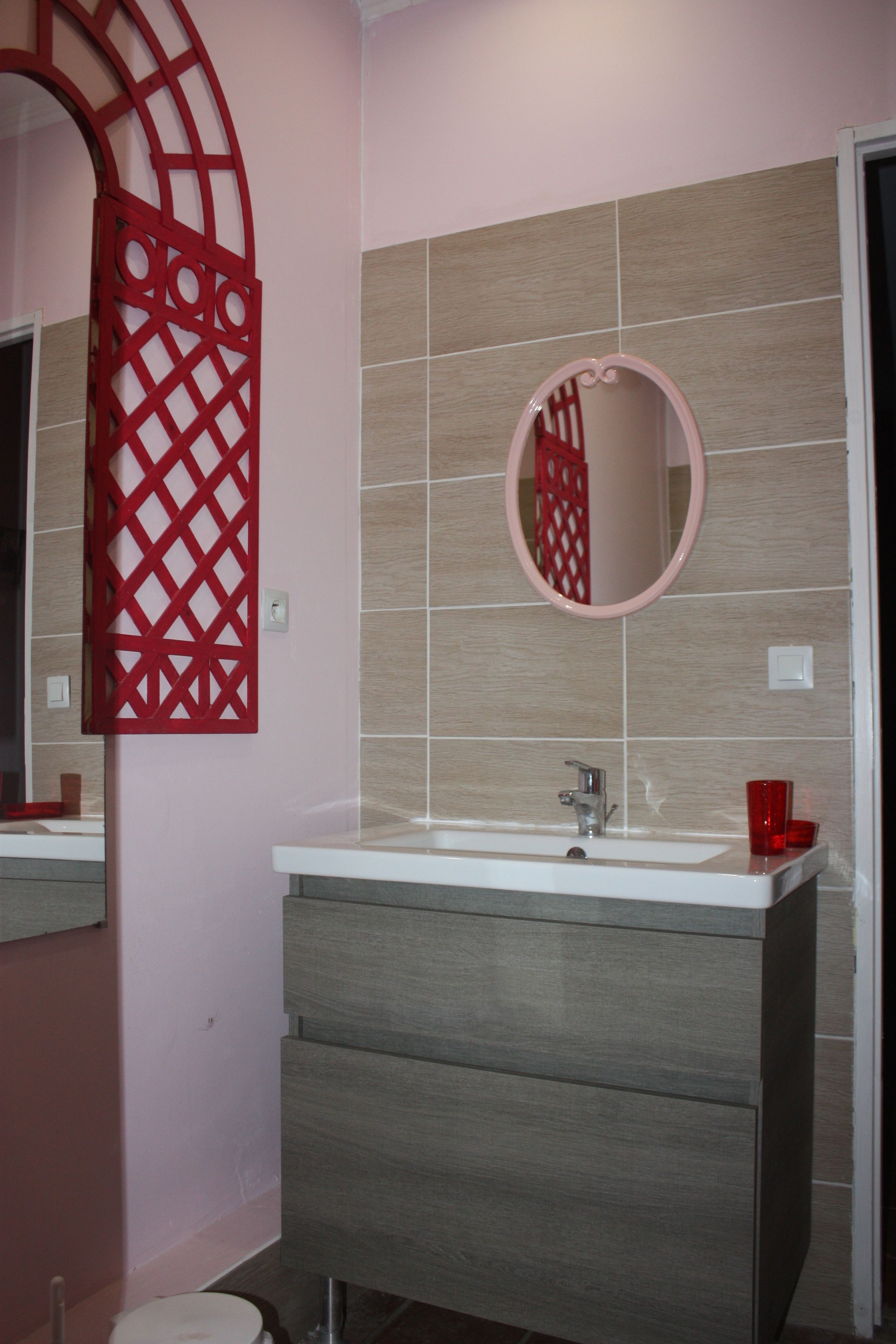 Un baño con tocador, lavabo, espejo y un panel decorativo rojo.