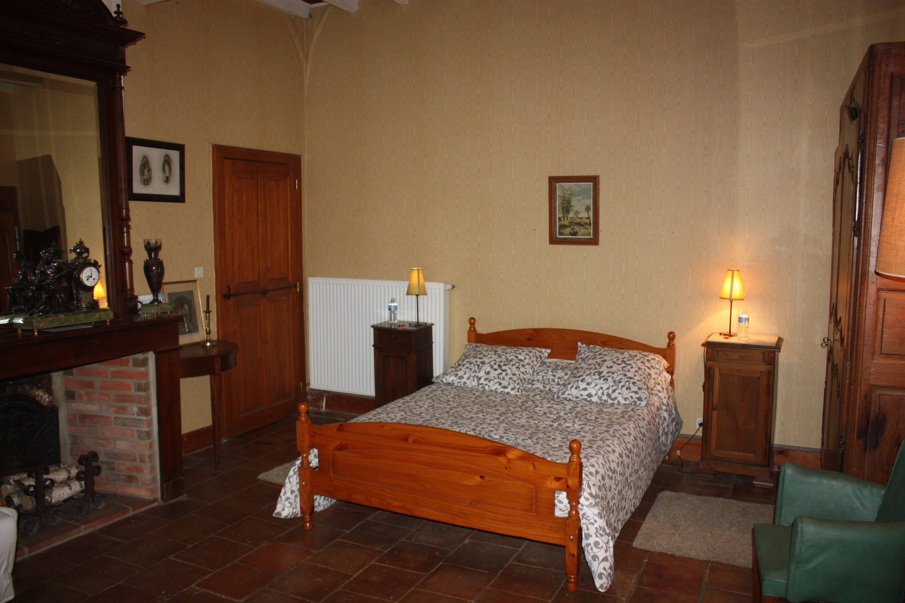 A bedroom with a wooden bed, a fireplace, a mirror, and a wooden wardrobe.