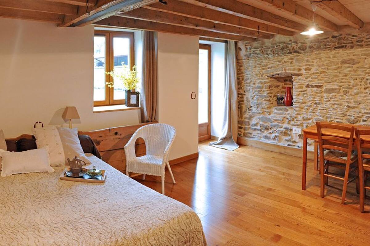 A bedroom with a bed, two chairs, a table, and a stone wall.