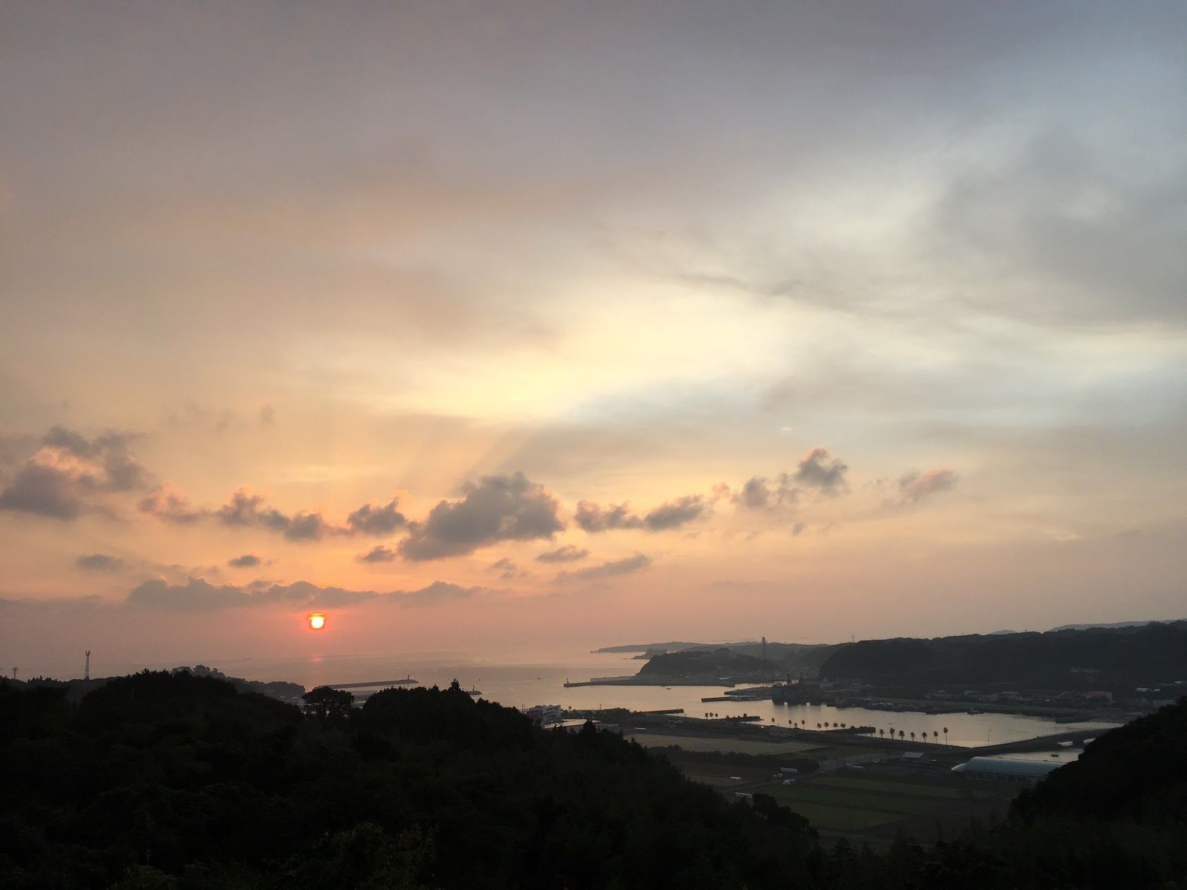 A coastal landscape with a sunset, hills, and a body of water.