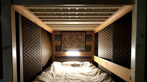 Habitación pequeña con cama individual, techo inclinado y paneles decorativos tejidos en la pared.