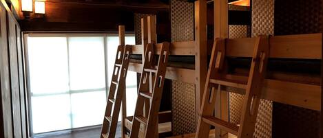 A room with wooden bunk beds, a woven wall, and a window with natural light.