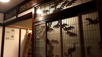 Ein traditioneller japanischer Raum mit Tatami-Boden, einem Shoji-Schirm mit Holzschnitzereien und einer Leiter zu einer erhöhten Ebene.
