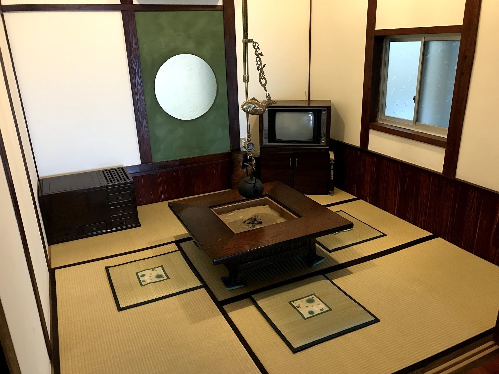 A tatami mat room with a traditional Japanese television, a decorative hanging, and a small table.