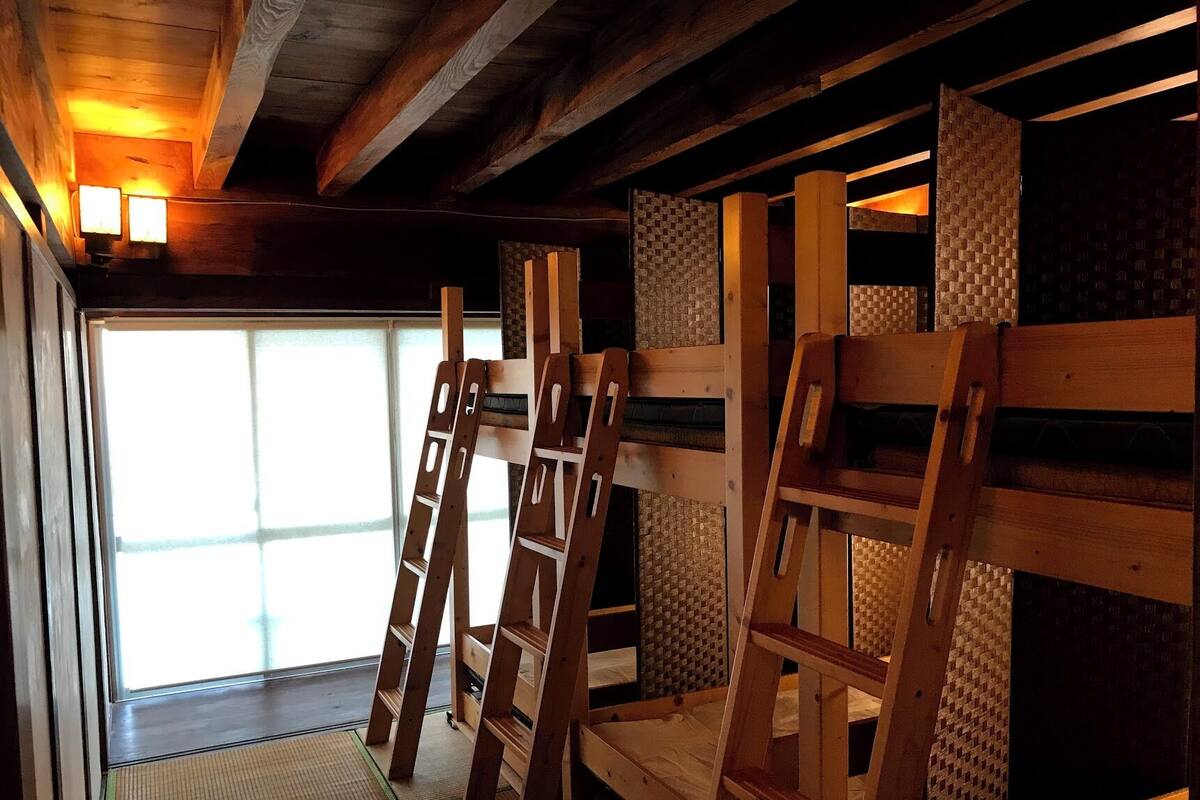 A room with wooden bunk beds, a woven wall, and a window with natural light.