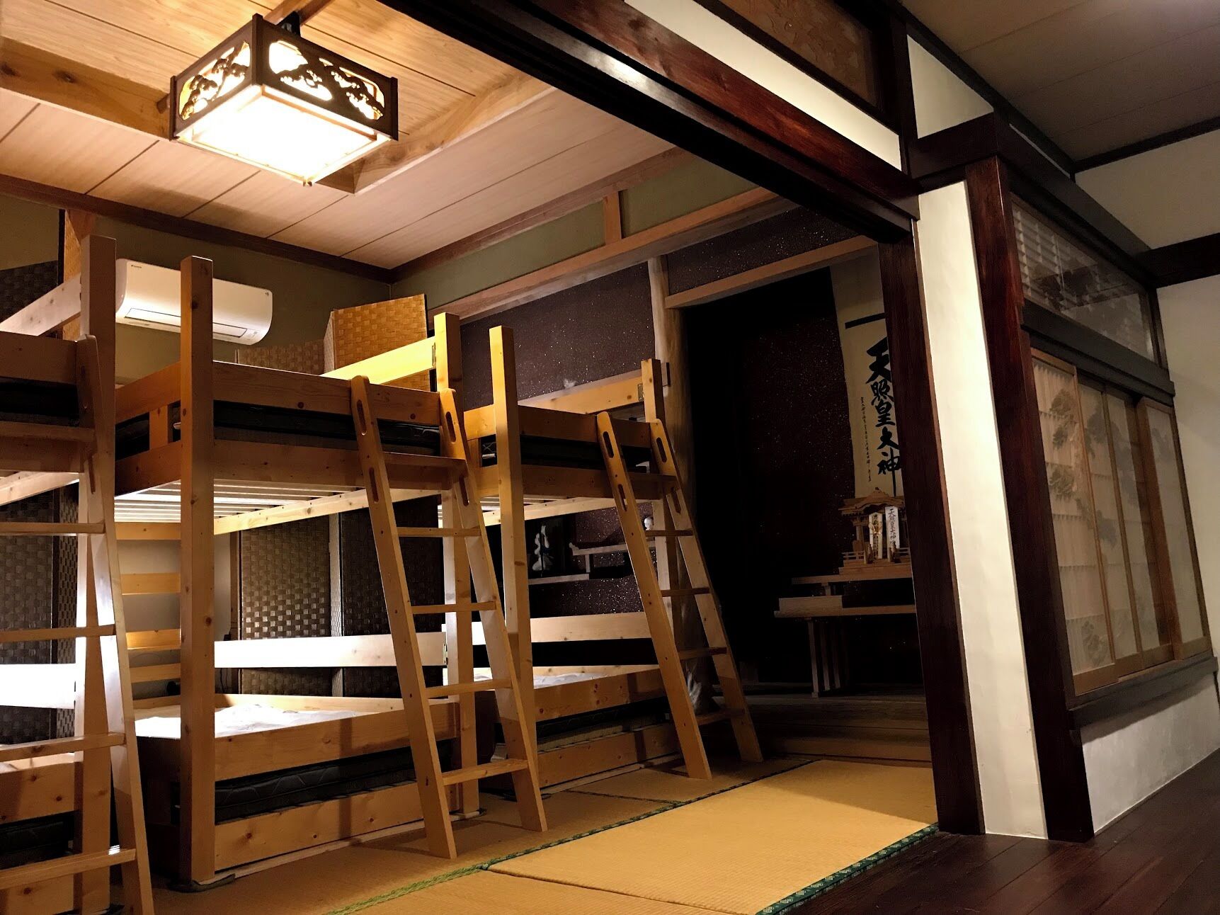 A traditional Japanese-style room with tatami flooring, wooden bunk beds, and a sliding door leading to another room.
