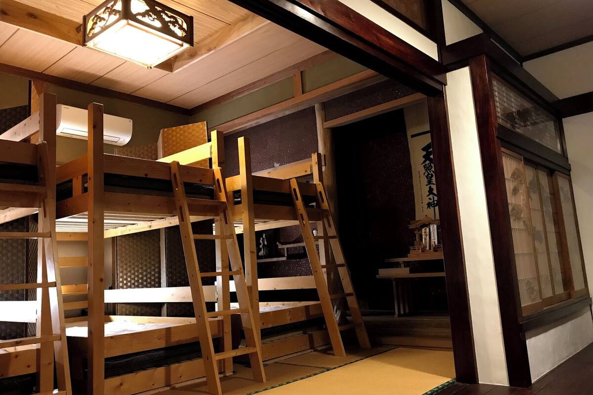 A traditional Japanese-style room with tatami flooring, wooden bunk beds, and a sliding door leading to another room.