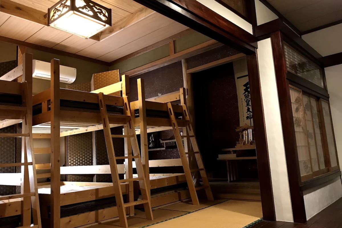 A traditional Japanese-style room with tatami flooring, wooden bunk beds, and a sliding door leading to another room.