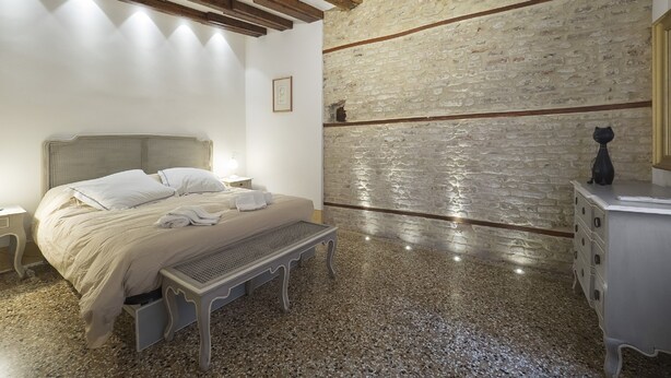 A bedroom with a bed, bench, dresser, and a stone wall. - Casa Margherita by Wonderful Italy (Venice)