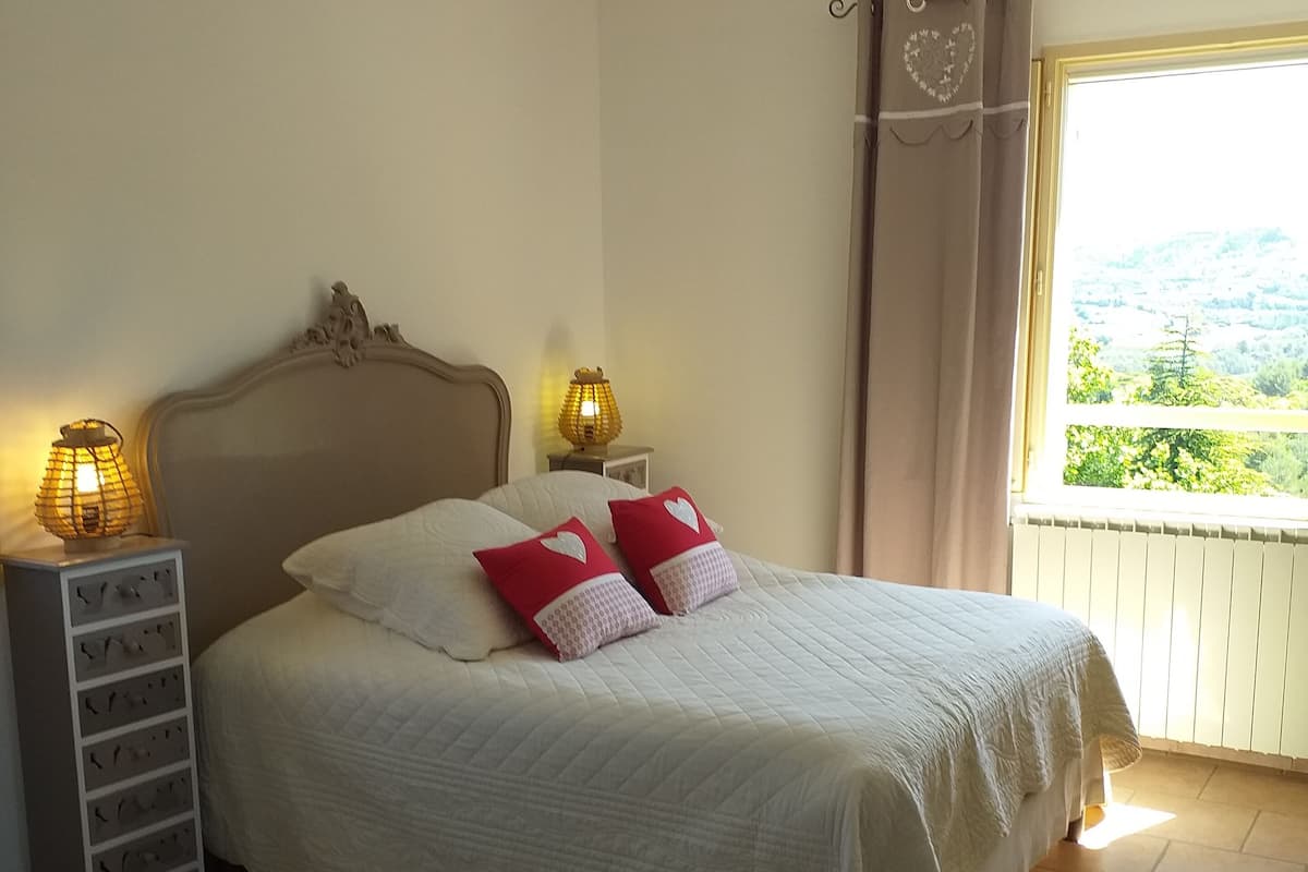 A neatly made bed with a headboard, two bedside lamps, and a view of a balcony with a railing.