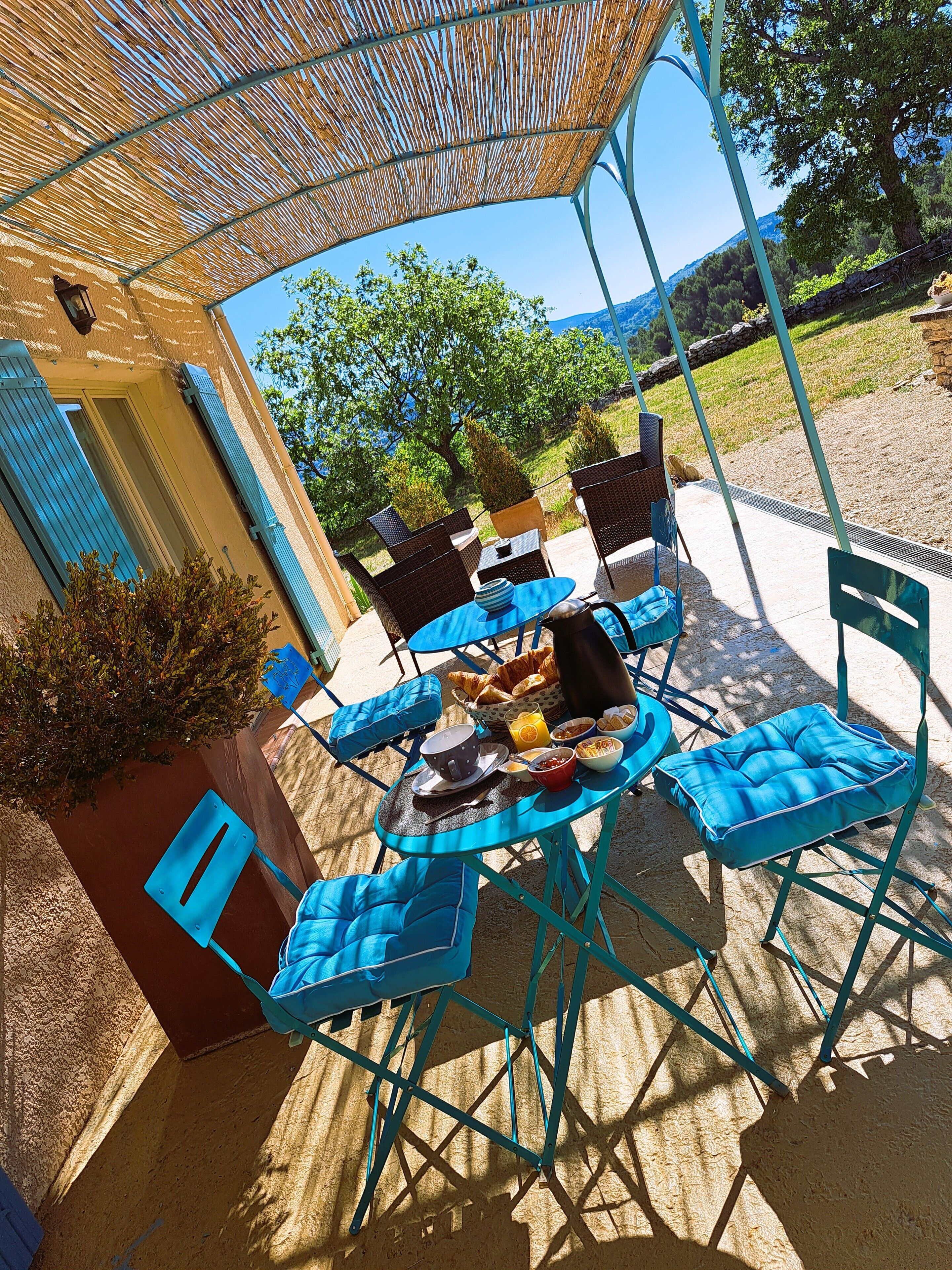 An outdoor seating area with blue chairs and a table set for breakfast, overlooking a scenic landscape.