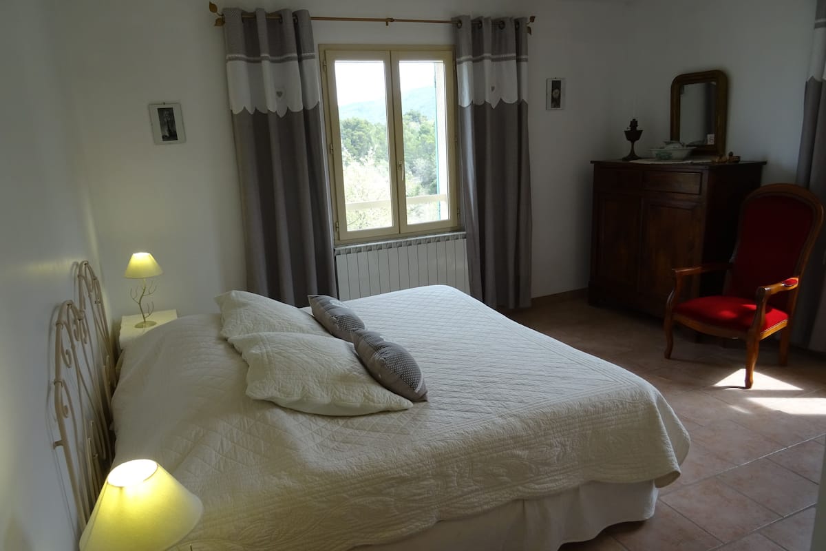 A bedroom with a bed, a chair, a dresser, and a window with curtains.