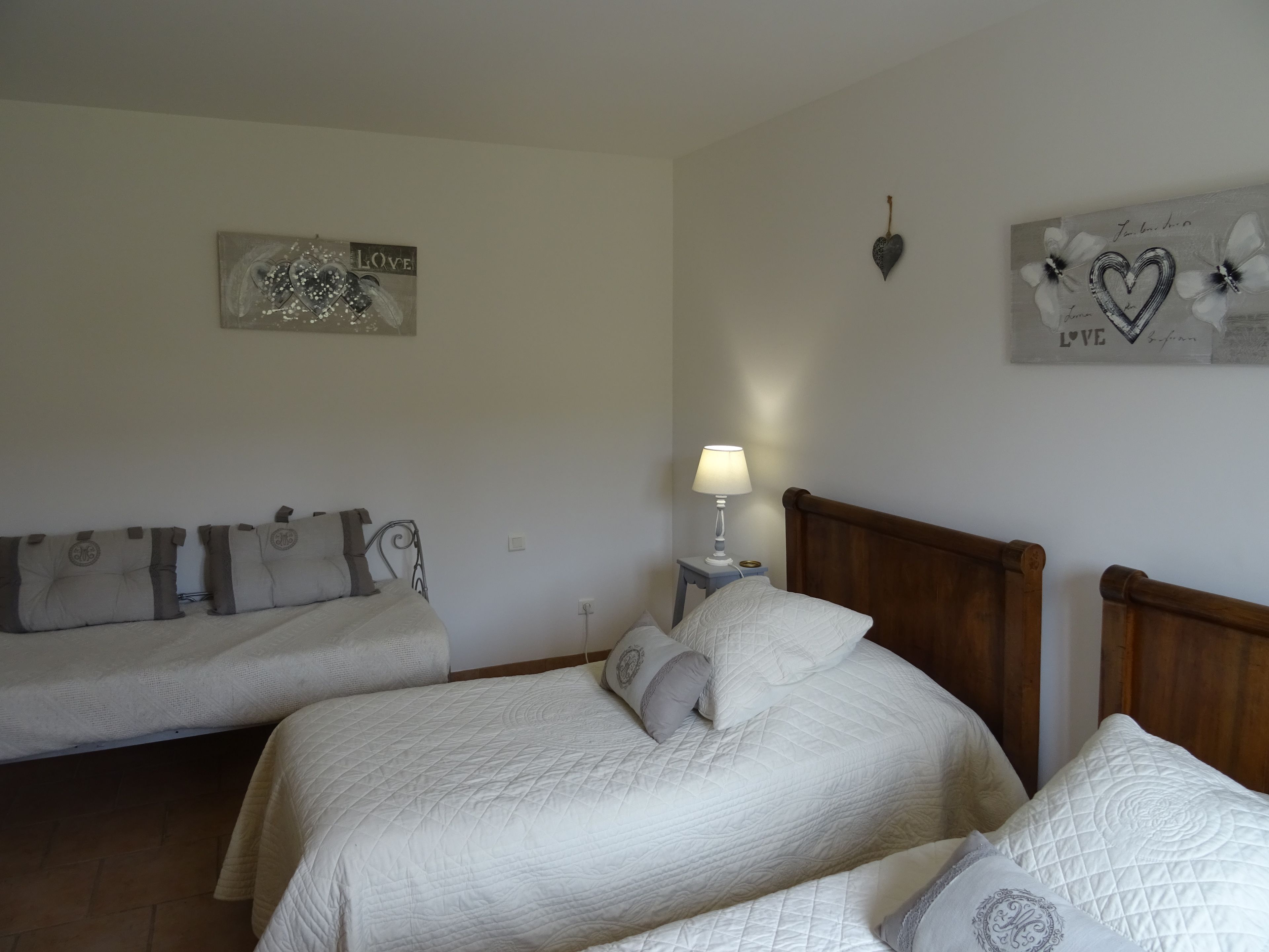 Une chambre avec deux lits, une table de chevet avec une lampe et des décorations murales, notamment un panneau avec le mot « Amour » et un élément décoratif en forme de cœur.