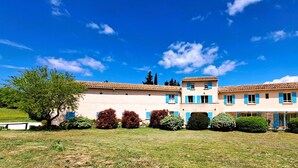A two-story building with a tiled roof, blue shutters, and a covered patio area. - Cante Grillet (Lacoste (Provence))