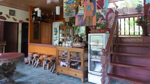 Een traditioneel houten interieur met een toonbank waarop diverse artikelen staan, een koelkast en een trap met een bordje.