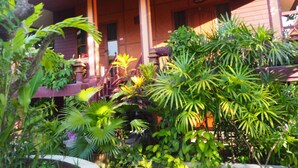 Een houten gebouw met een overdekte veranda en weelderige tropische planten op de voorgrond.