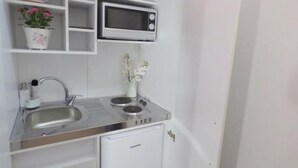 Una kitchenette compacta con microondas, dos fregaderos, un refrigerador pequeño y objetos decorativos en los estantes.