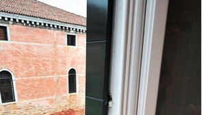 A window with a view of a canal and a boat, a cup and saucer, and orange placemats on a table. - Vivaldi room - Biennale by Wonderful Italy (Venice)