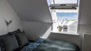 A bedroom with a skylight, a bed with patterned bedding, a potted orchid, and a view of the sea. - Samsø Perlen (Samsø)