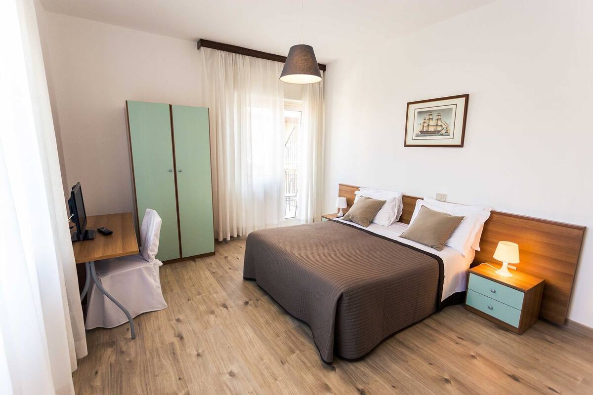 Une chambre d’hôtel comprenant un lit, une table de chevet, une lampe, une armoire et un bureau avec une chaise.