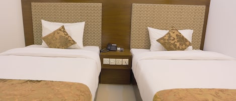 A hotel room with two beds, each with a patterned headboard and matching pillows. There is a bedside table with a phone and a power outlet.
