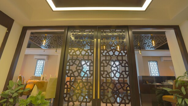 A modern interior with a geometric patterned door, a ceiling light fixture, and a dining area with chairs and a table. - Holy Inn (Sylhet)