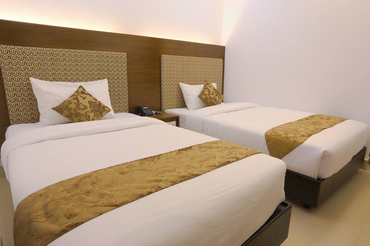 Ein Hotelzimmer mit zwei Betten, jeweils mit einem gemusterten Kopfteil und einem Nachttischchen mit Telefon.