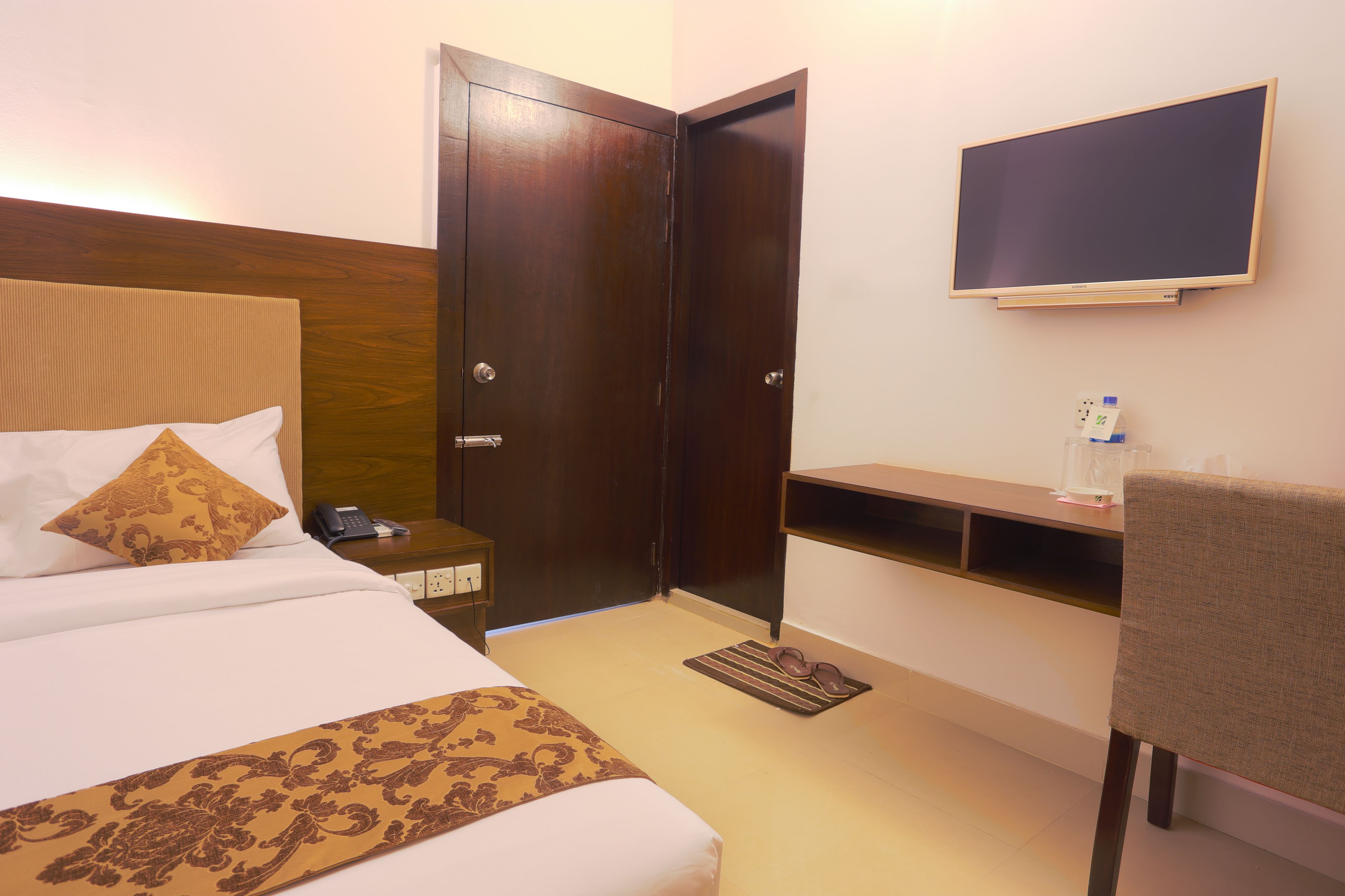 A hotel room with a bed, bedside table, TV, and a chair.