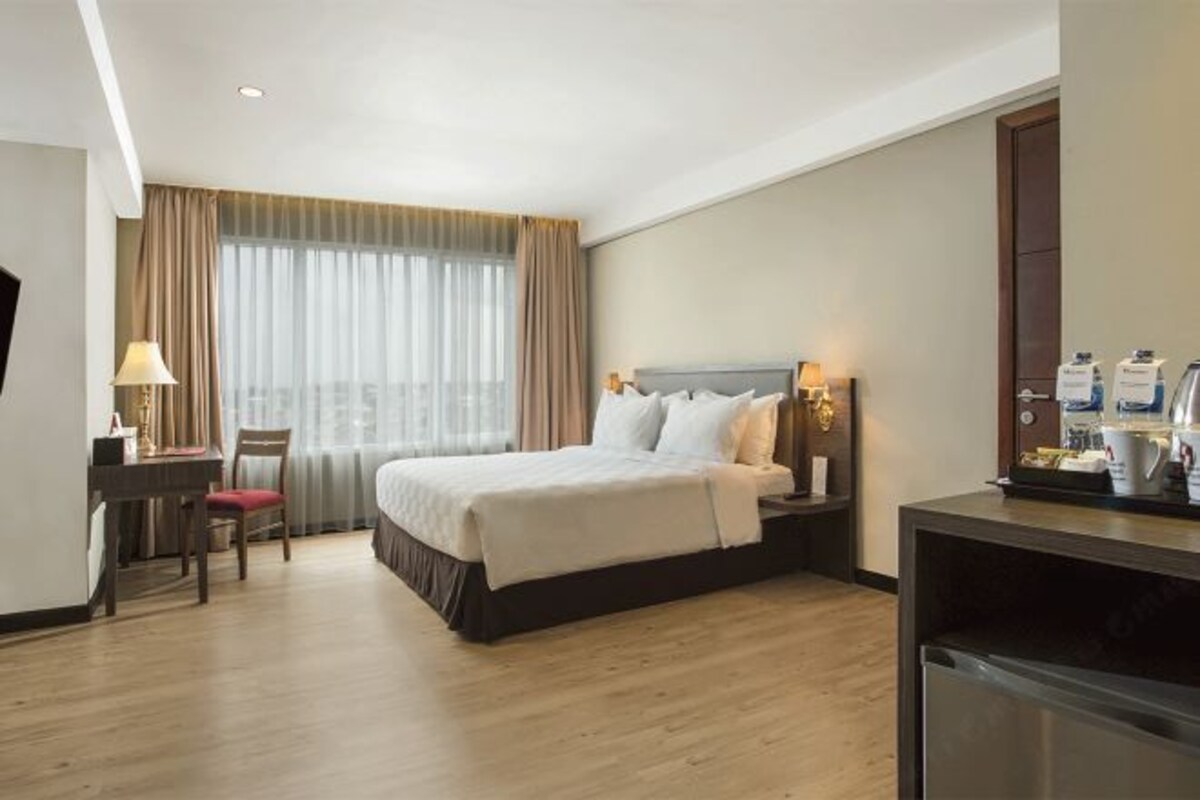 A hotel room with a bed, bedside table, lamp, and a desk with a chair.