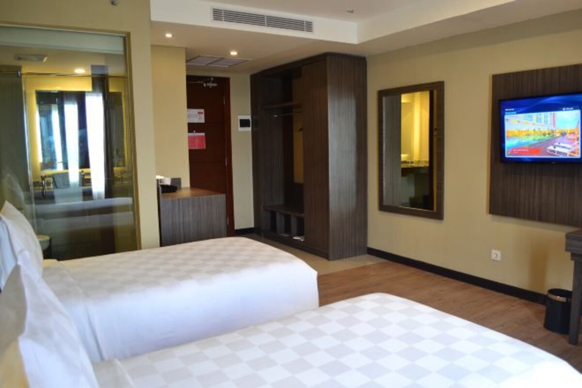 A hotel room with two beds, a television, and a mirror.