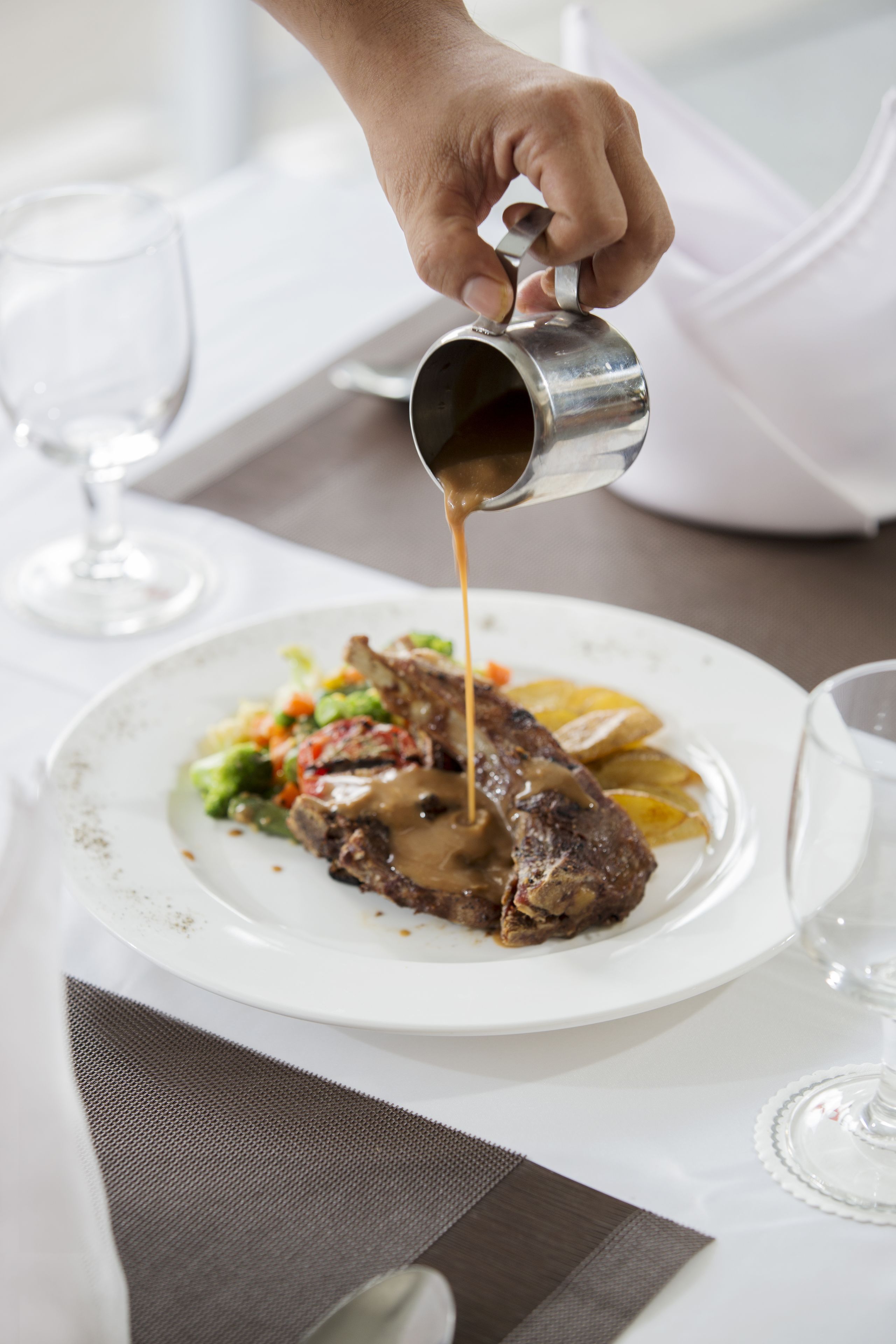 Una persona sirviendo salsa sobre un bistec en un plato.