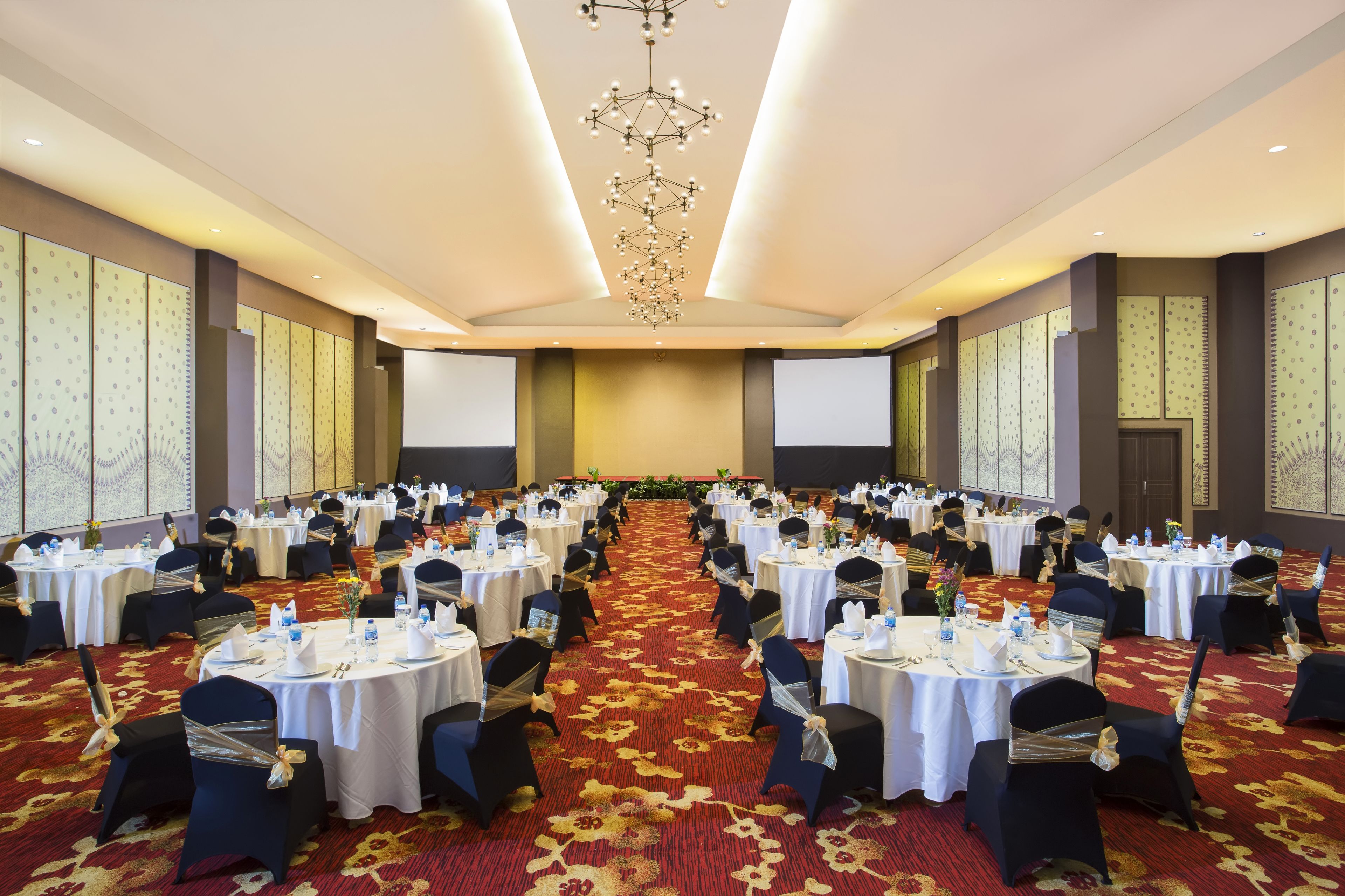 A large conference room with round tables, black chairs, and a red carpet.