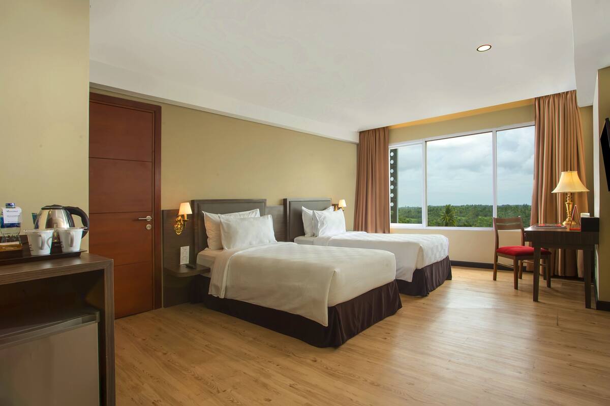 A hotel room with two beds, a desk, a chair, a TV, and a window with a view.