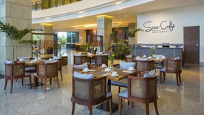 Un vestíbulo amplio con varias mesas y sillas para comer, un restaurante visible llamado 'Swiss Café' y una barandilla decorativa en el nivel superior.