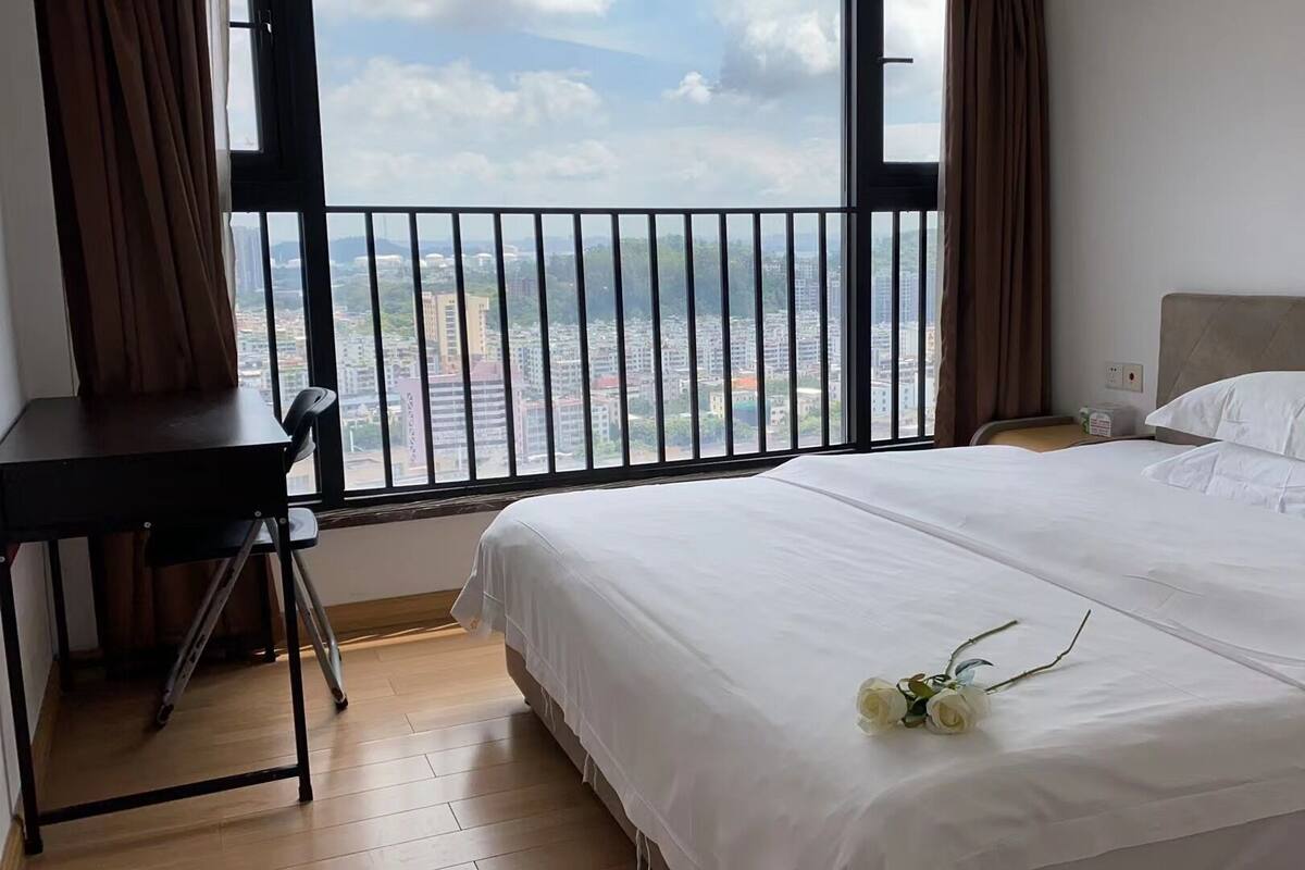 Une chambre d’hôtel avec une grande fenêtre, un lit avec une literie blanche, un bureau et une chaise.