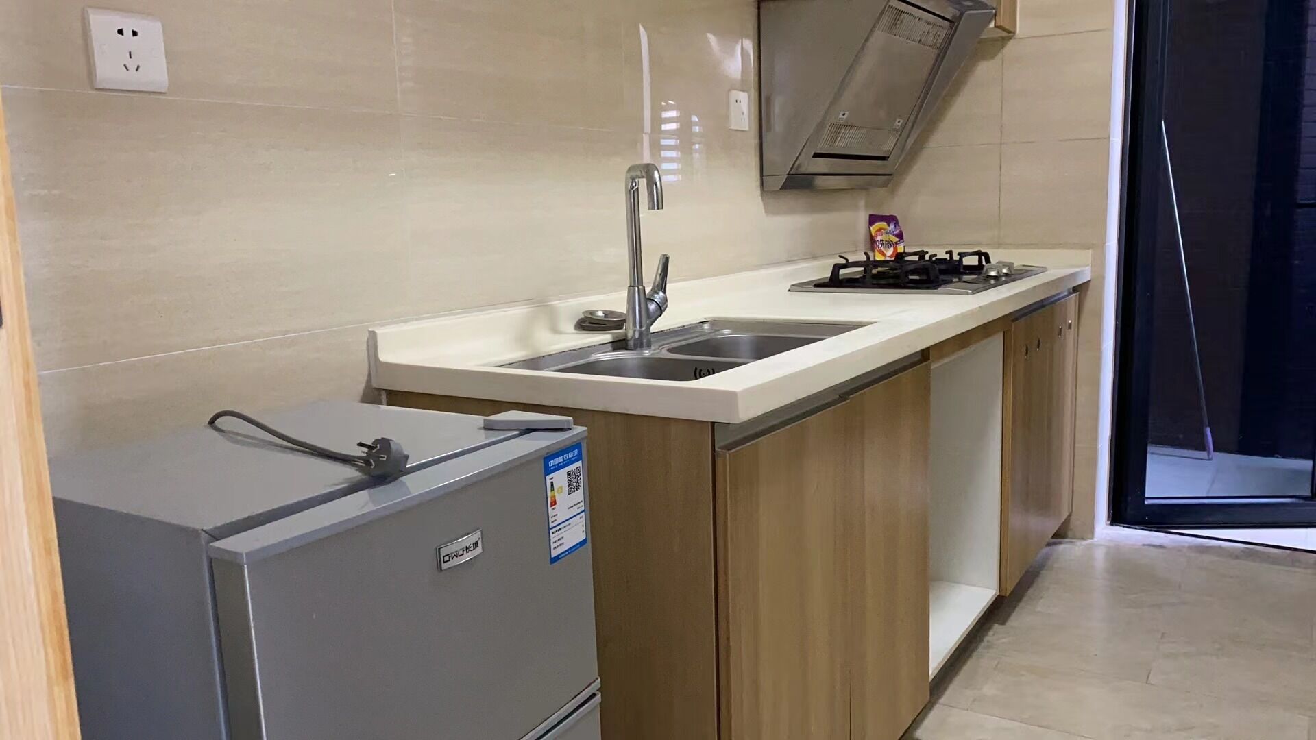 Une cuisine de taille réduite, équipée d’une cuisinière à gaz intégrée, d’un évier et d’un réfrigérateur compact.