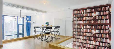 A modern interior with a dining area, a large bookshelf, and a view of the city through a large window.
