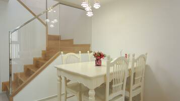 A dining area with a white table and chairs, a vase with flowers, and a staircase with wooden steps.