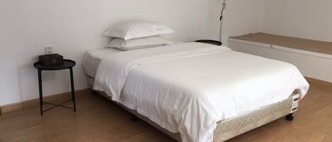 A neatly made bed with white bedding, a small bedside table, and a wall-mounted lamp.